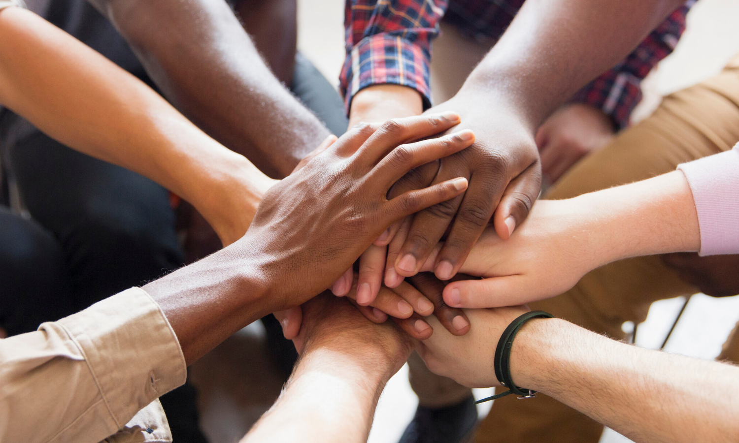 A close up of multiple hands of diverse skin tones held together in a circle